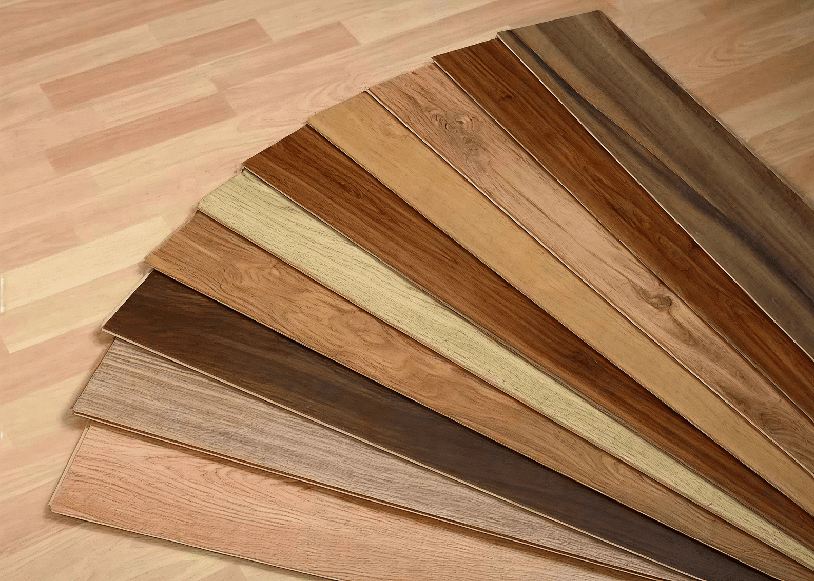 A fan of wooden flooring samples in various shades from light oak to dark walnut is displayed against a wooden floor background, showcasing texture and color variety.