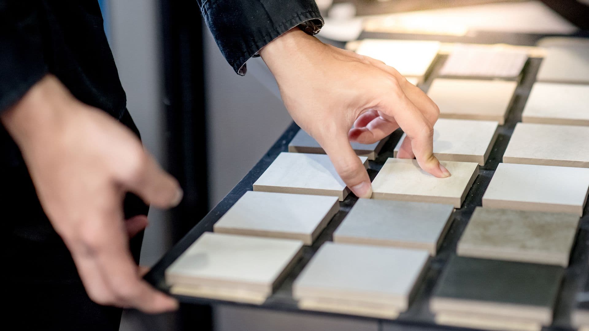 A person in a dark jacket selects a tile sample from an organized display of various color tiles, conveying choice and interior design elements.