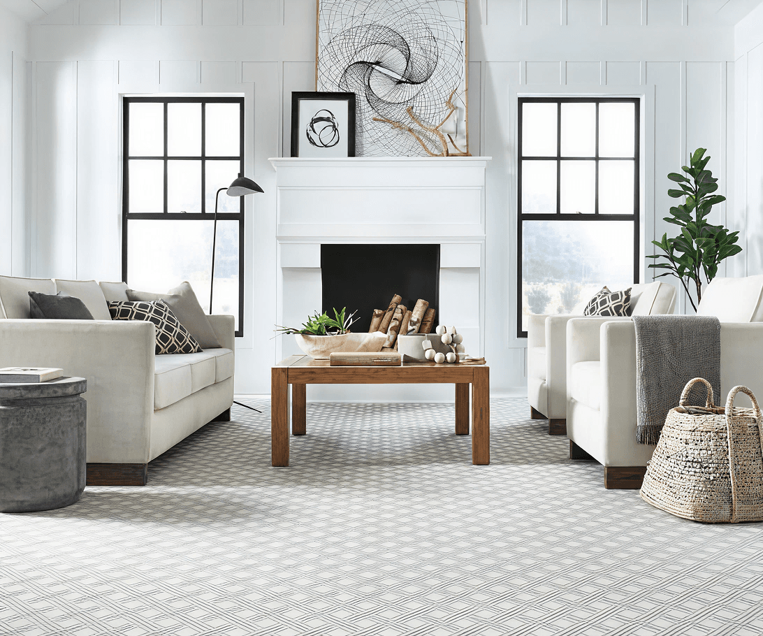 Bright living room with two white sofas facing a wooden coffee table. A modern fireplace is centered between two windows. Neutral tones create a calm ambiance.