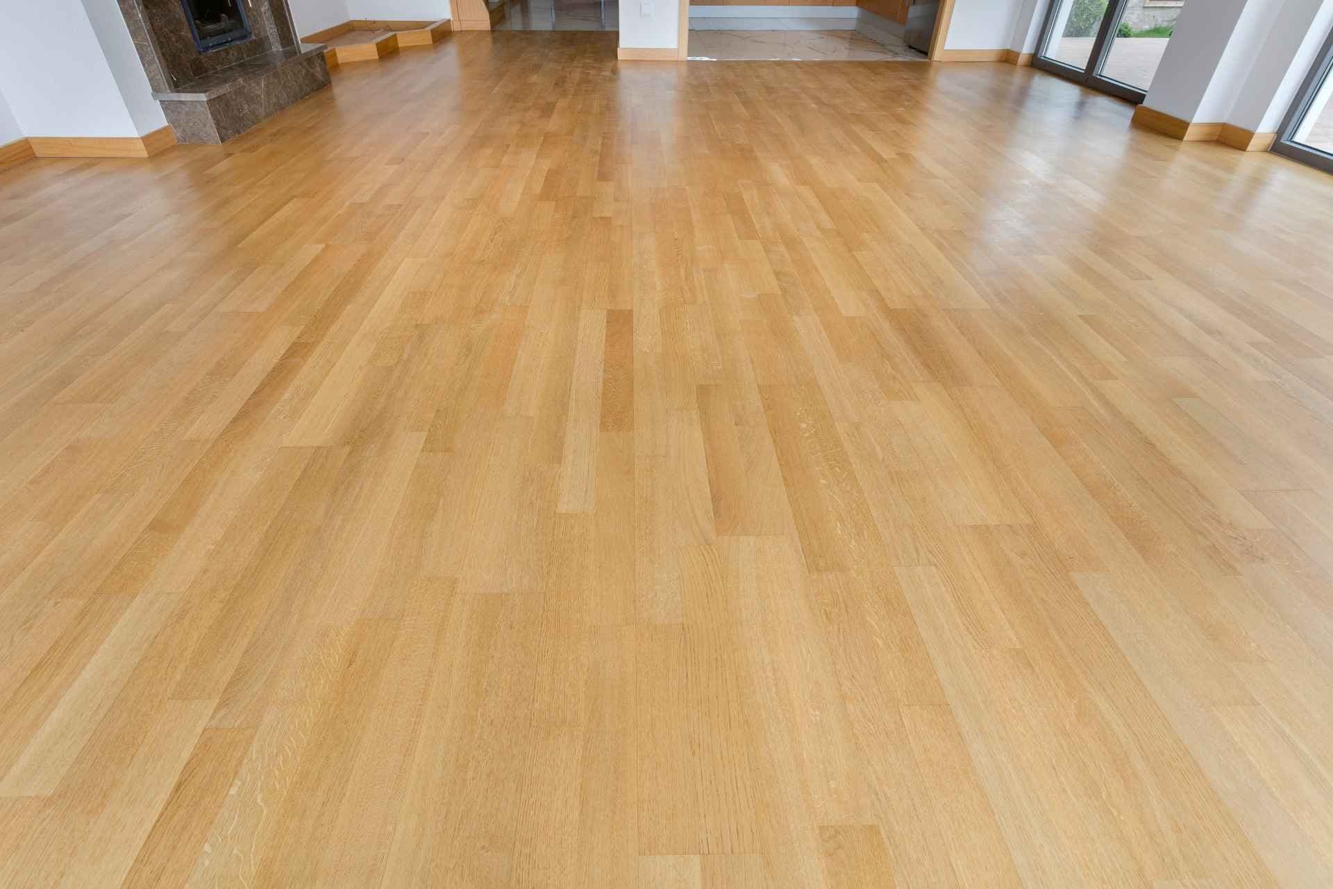 Spacious room featuring polished light wood flooring. The room is bright, with large windows on the right, white walls, and a stone fireplace on the left.