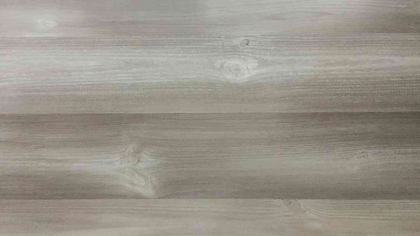 A close-up of a light gray wooden surface with visible grain patterns and knots. The texture suggests a natural and rustic tone.