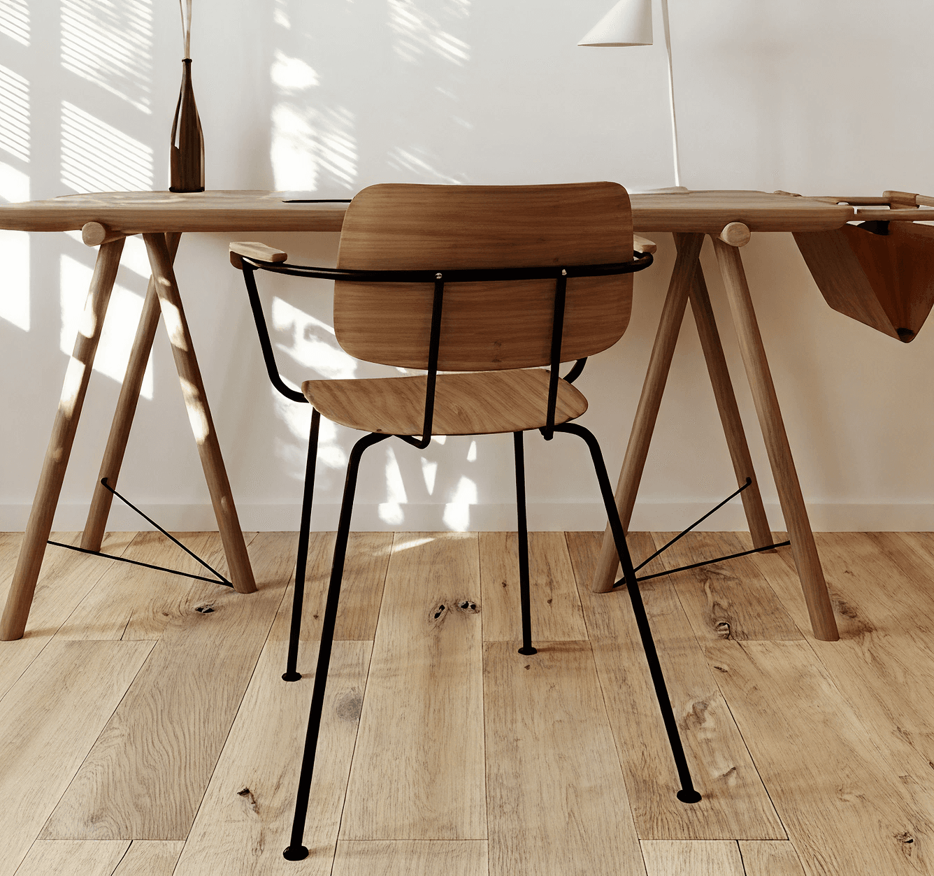 A wooden chair with black metal legs sits at a minimalist desk in a sunlit room. A vase and lamp adorn the desk, and sunlight casts patterns on the floor.