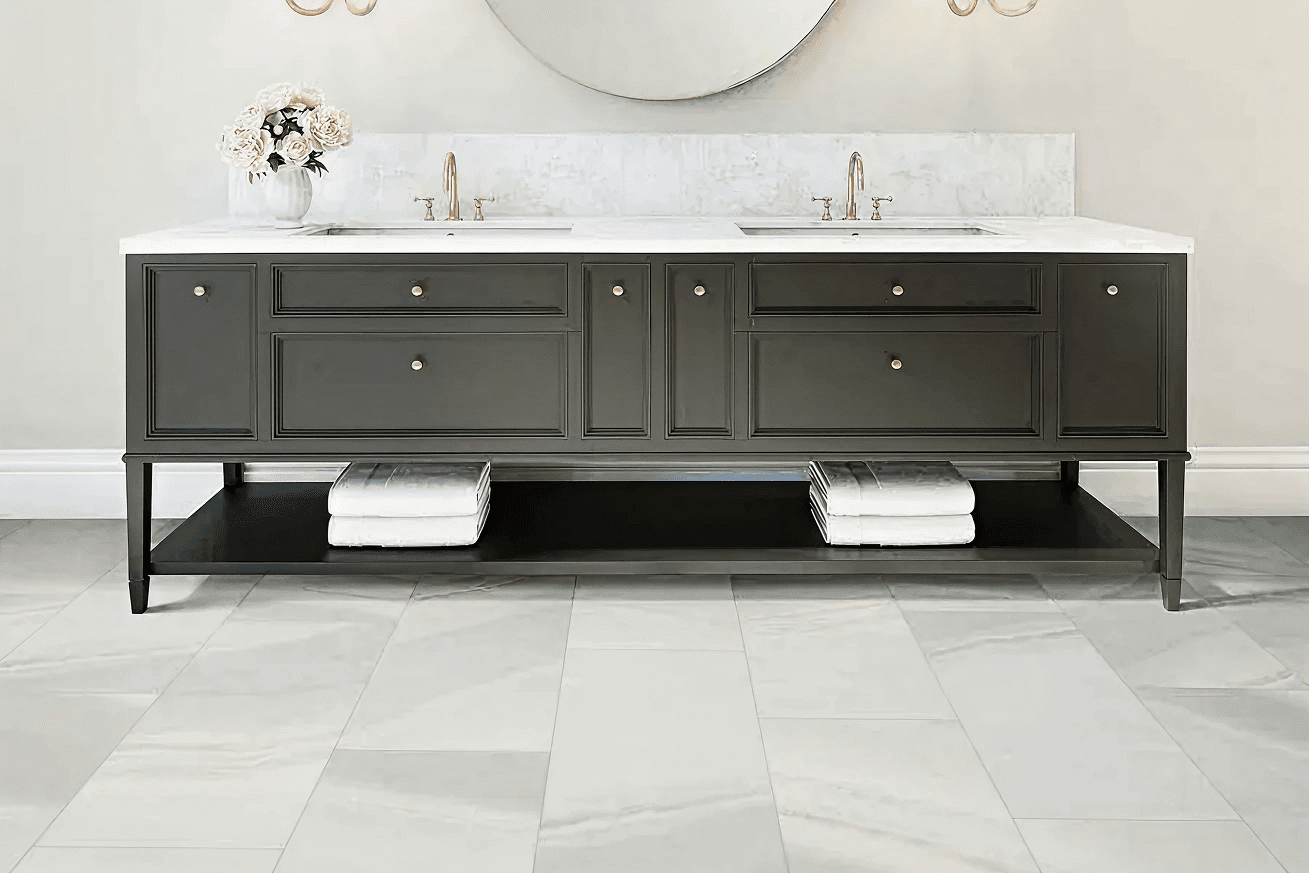 Elegant bathroom vanity with dark cabinets, dual sinks, a white marble countertop, and gold fixtures; decor includes a vase of flowers, evoking a serene feel.
