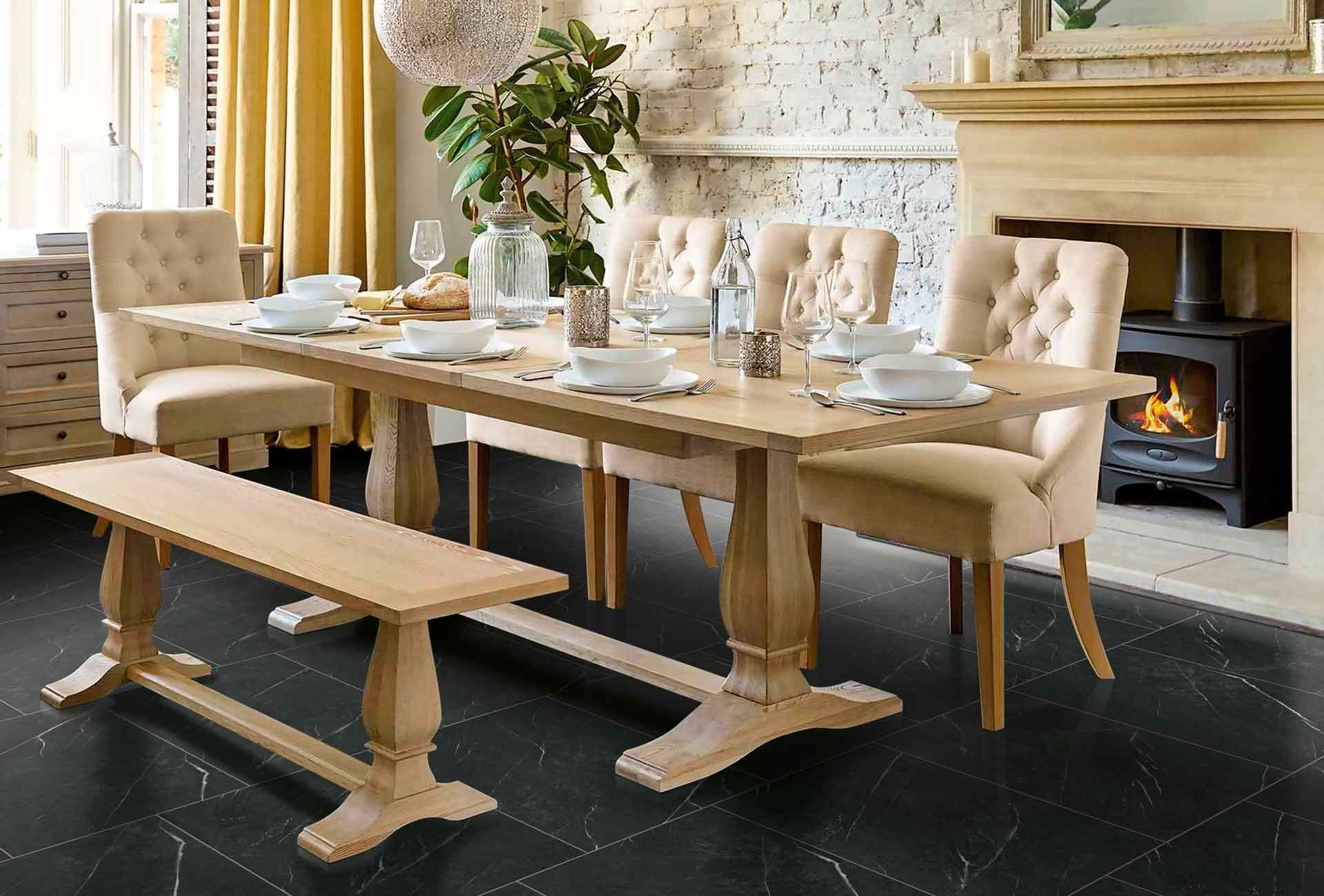 Elegant dining room with a wooden table set for six, featuring beige chairs and a bench. A cozy fireplace and potted plant create a warm ambiance.