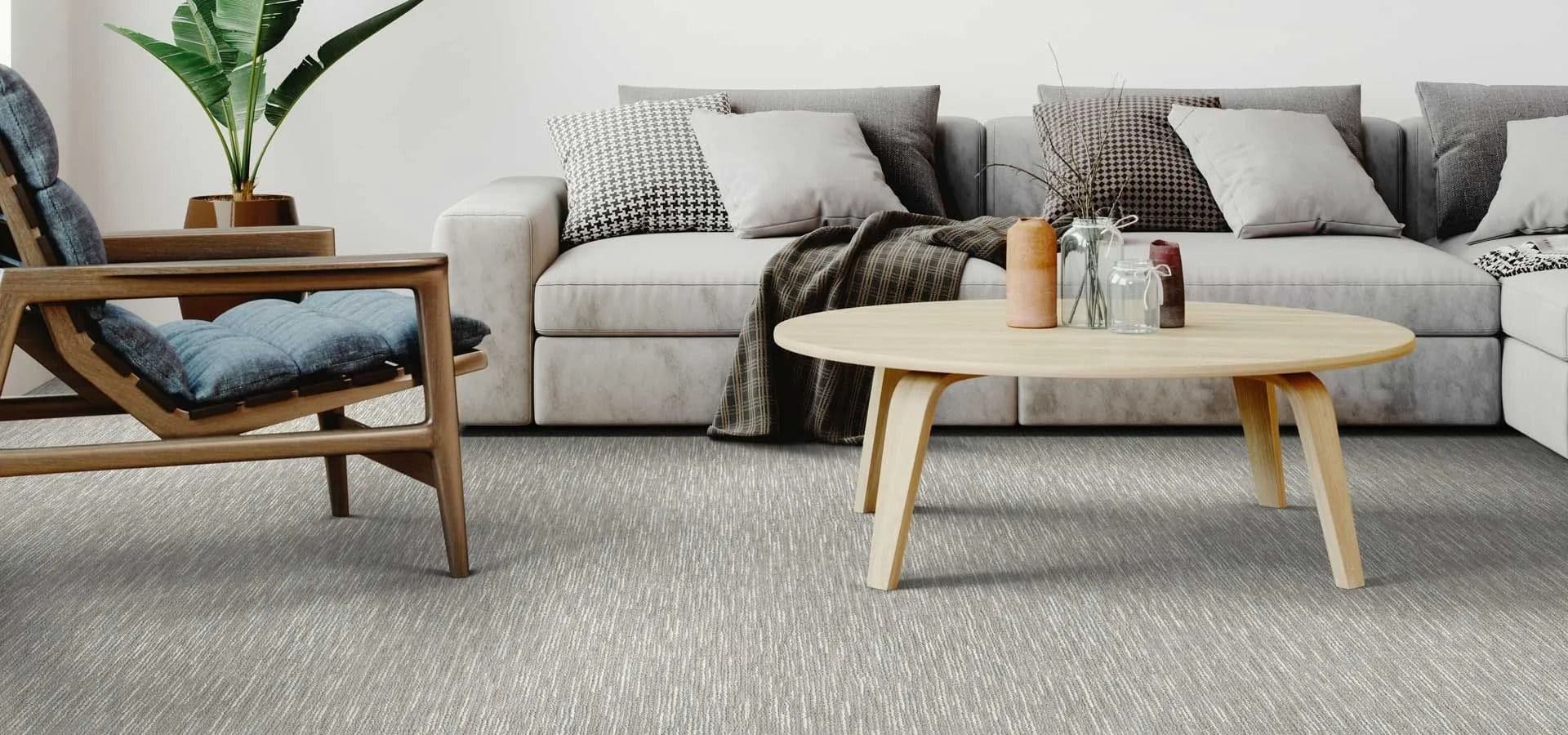 A modern living room with a beige sofa, assorted pillows, and a cozy plaid throw. A wooden coffee table and potted plant create a welcoming atmosphere.