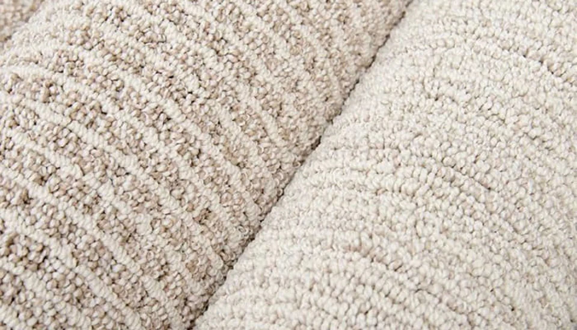 Close-up of two rolls of textured beige carpet placed side by side. The surface displays a subtle pattern, conveying a sense of warmth and coziness.