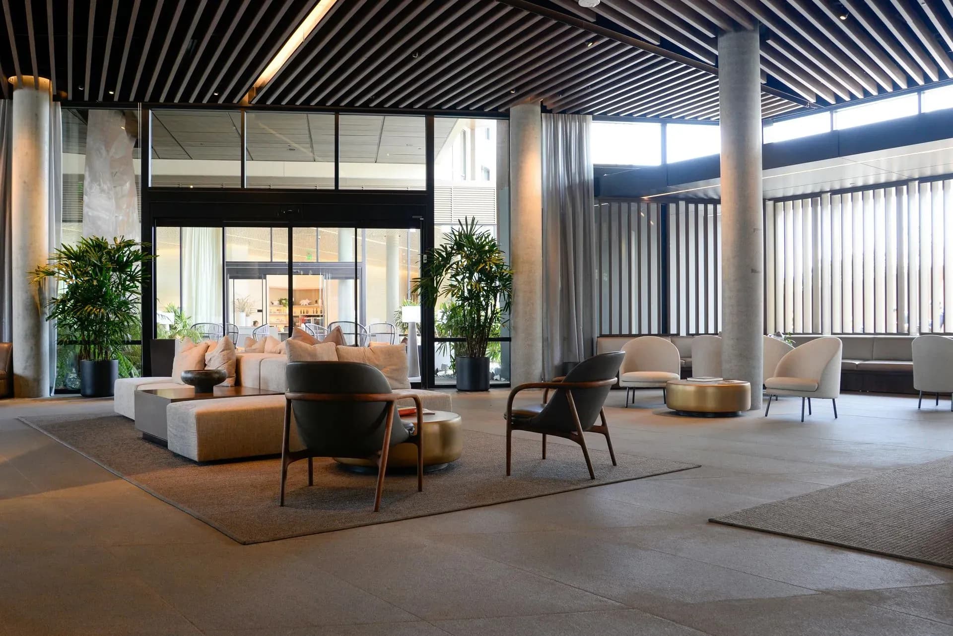 Modern hotel lobby with sleek furniture, large glass doors, and natural light. Neutral tones and indoor plants create a calm, welcoming atmosphere.