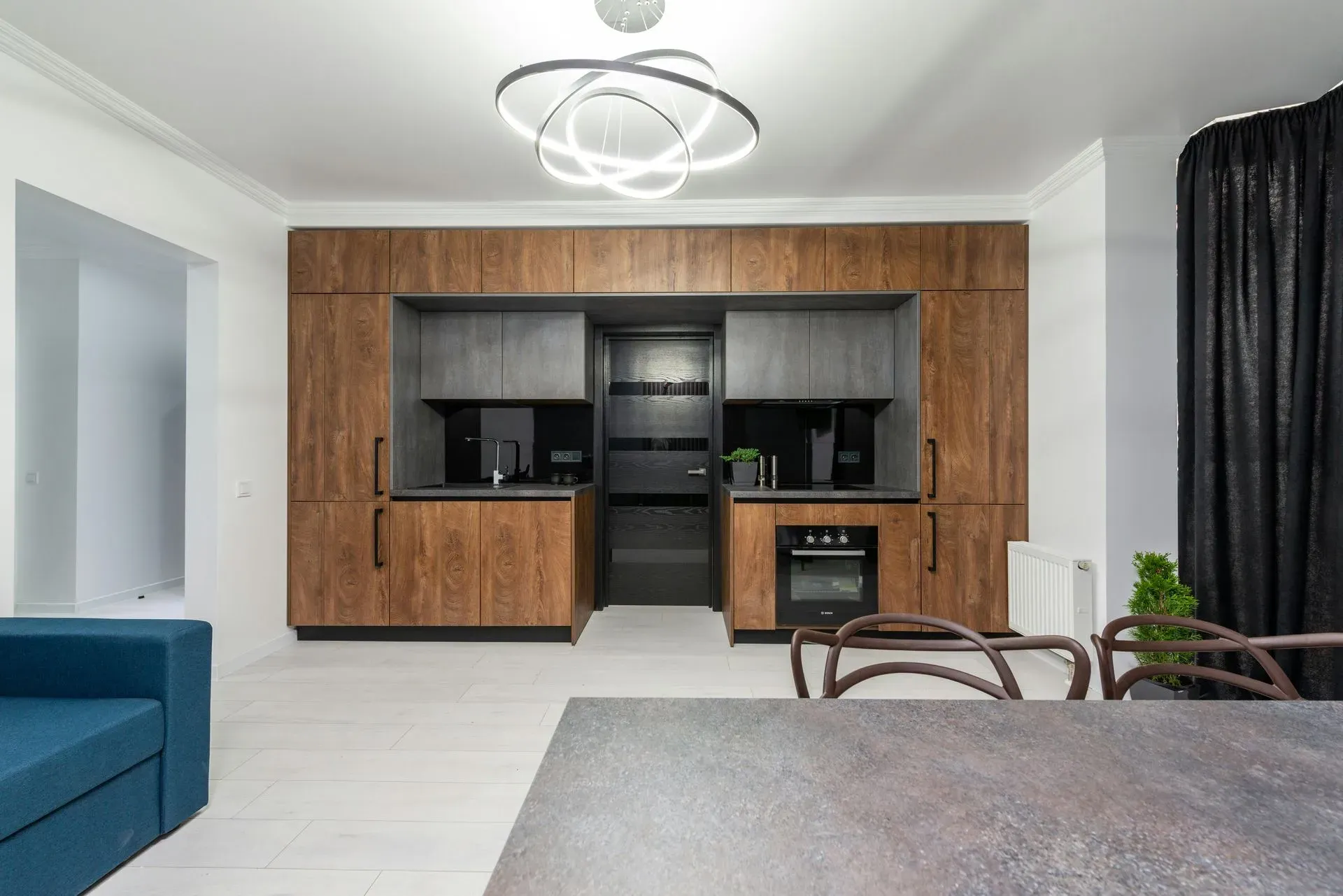 Modern kitchen with wood cabinetry, black countertops, and built-in appliances. A sleek circular light fixture hangs above. The space feels contemporary and elegant.
