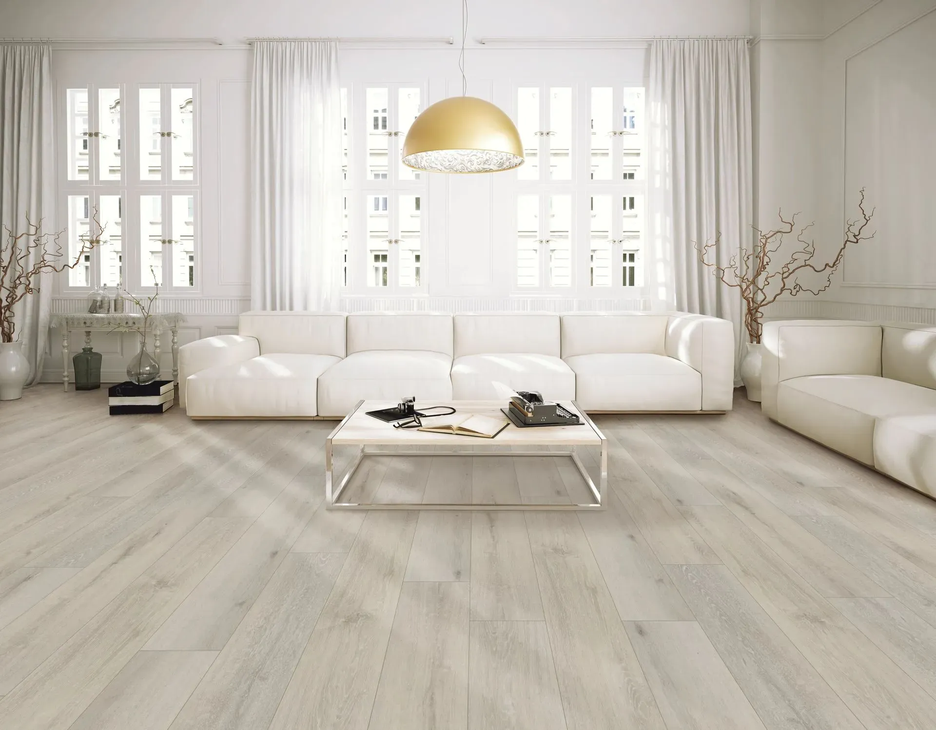 Spacious living room with white sofas, a large gold pendant light, and a minimalist coffee table. Ample windows and light wood floors create an airy feel.