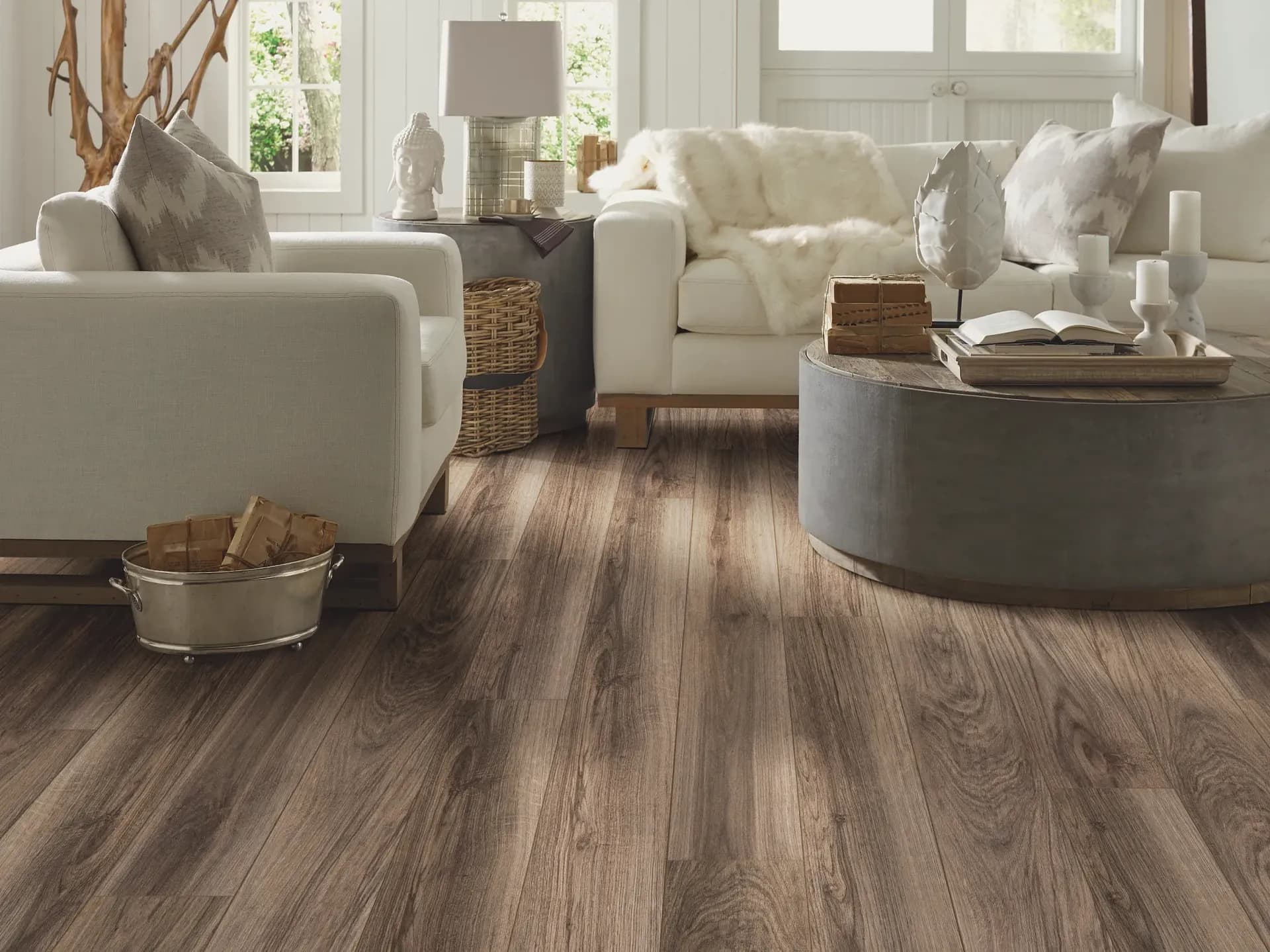 Cozy living room with light sofas, a round gray coffee table, and decorative elements. Warm wood floors enhance the inviting, peaceful atmosphere.